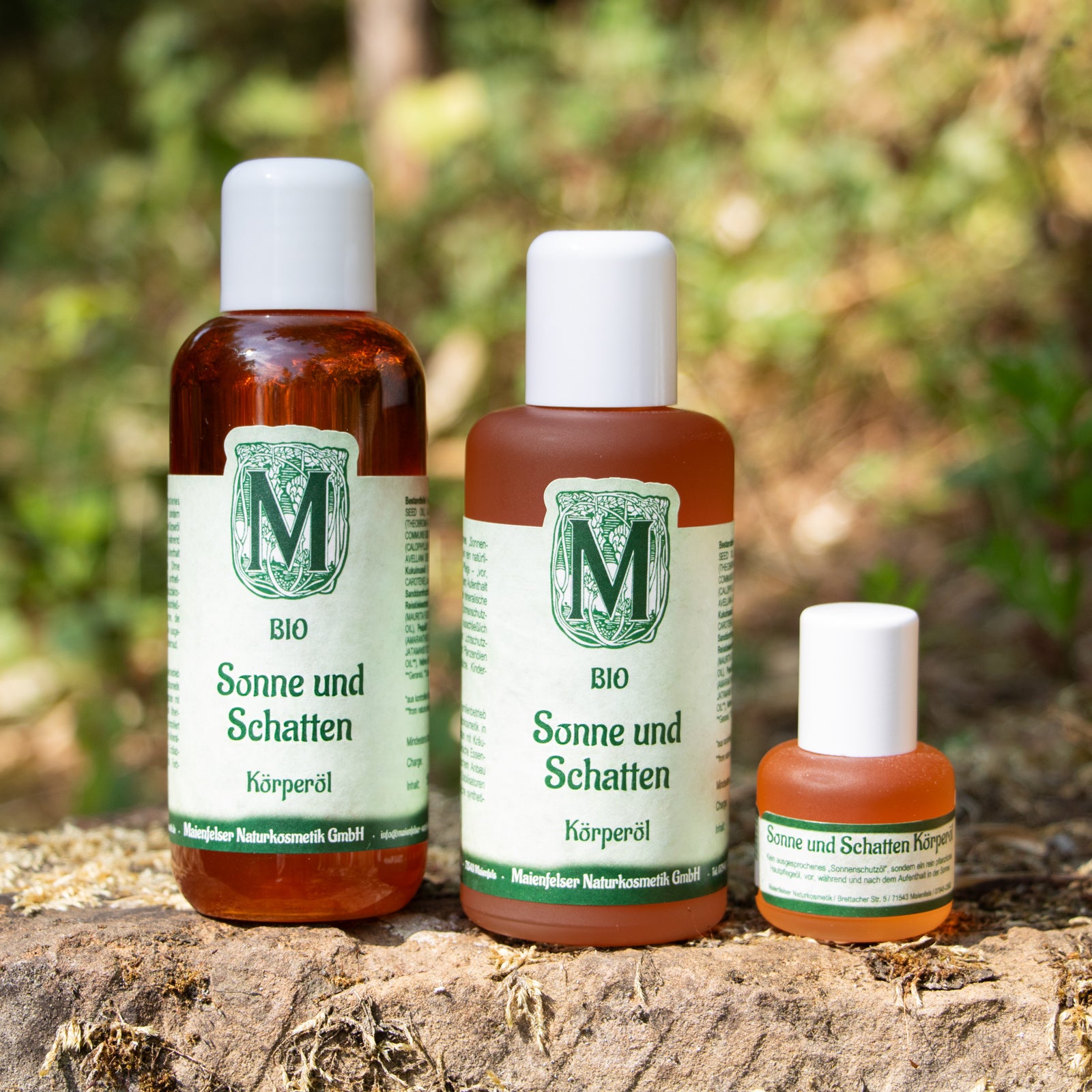 Sonne und Schatten Körperöl in 100ml und 15ml Abfüllgröße, abgestellt vor grünen Blättern und Gräsern